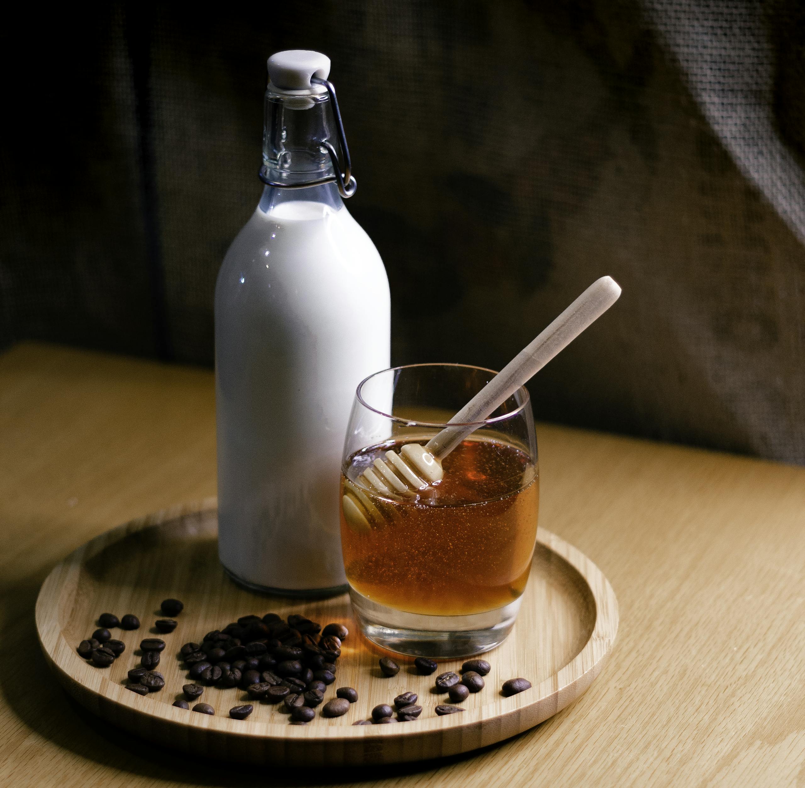 Elegant setup featuring a milk bottle and honey glass on a wooden tray with coffee beans.